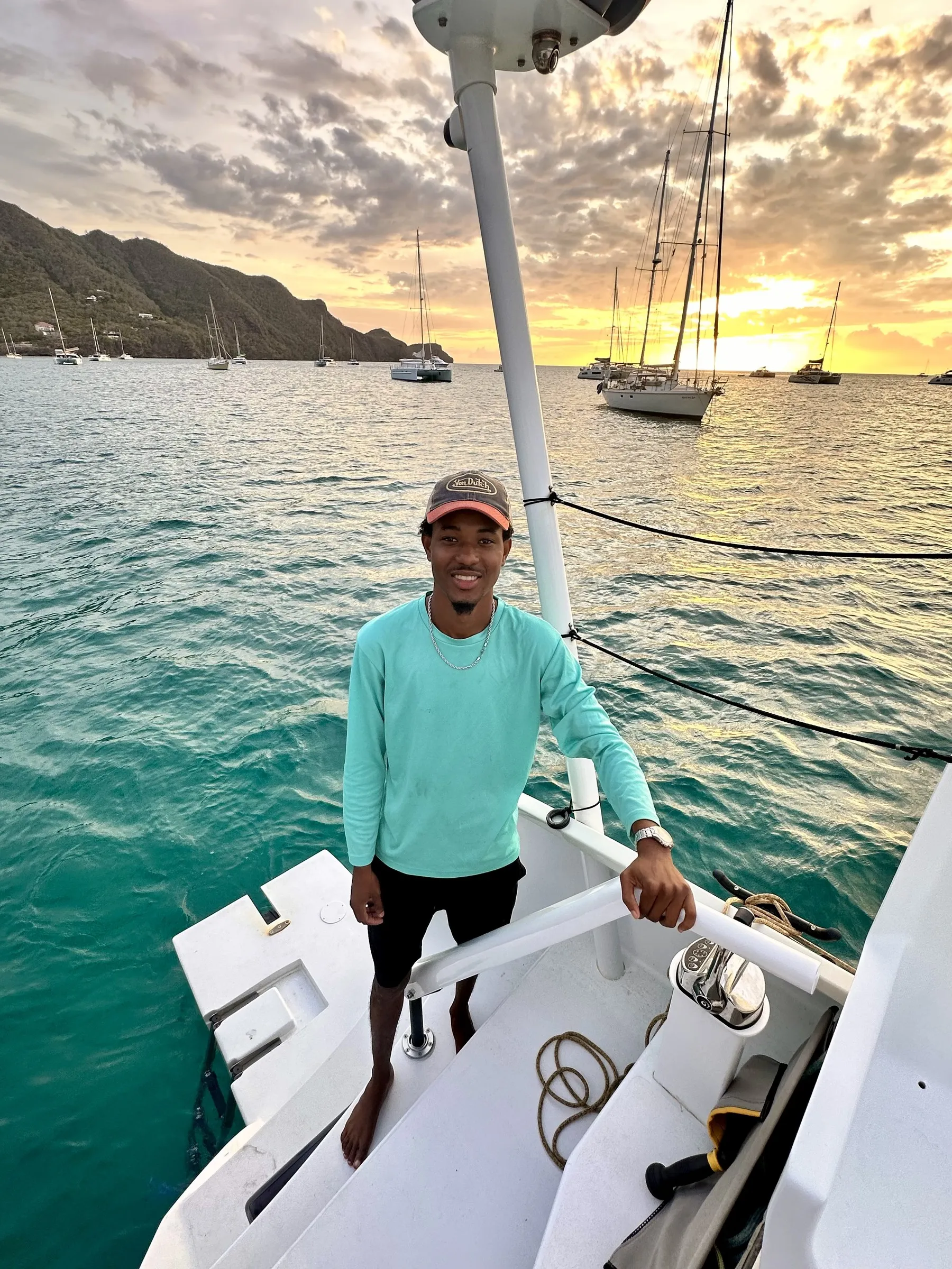Terrel Andrews, White Dog Sailing's skipper, standing on the bow of a catamaran at sunset